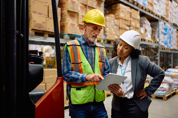 Senior worker and warehouse manager cooperating while using touchpad in storage compartment.