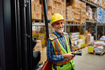 Happy senior forklift operator working at distribution warehouse and looking at camera.