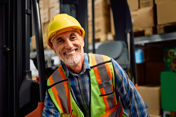 Happy senior forklift operator in warehouse looking at camera.