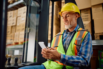 Happy forklift operator using cell phone at distribution warehouse. © Drazen