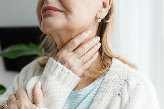 Closeup cropped image of unrecognizable aged female touching her throat being sick, feeling unwell, concerned of her thyroid dysfunction and pain, having endocrine disease of typical flue
