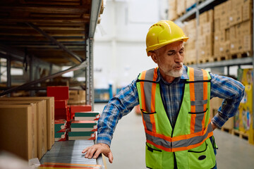 Senior worker feeling pain in his back while working at distribution warehouse.