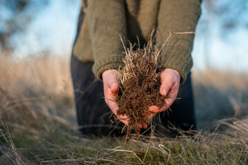 female soil scientist agronomist farmer looking at soil samples and grass in a field in spring....