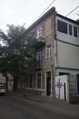 Low-angle view of a weathered brick building in Tbilisi, Georgia, featuring a unique purple graffiti mural.  The architecture showcases old-world charm and urban decay.
