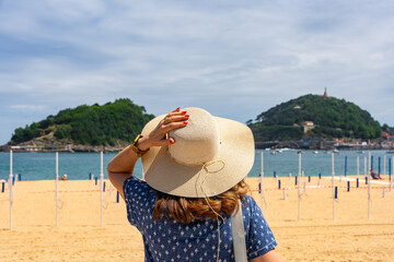 Tourist woman with hat on her back next to Ondarreta beach in San Sebastian, Basque Country.