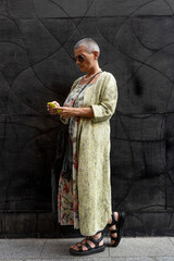 elegant smiling mature woman with shaved grey hair texting on cell phone in front of black wall