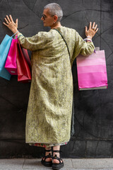 elegant mature woman with colorful shopping bags posing with her back turned in front of a black wall