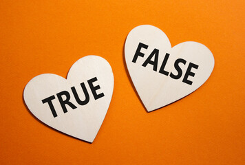 True or False symbol. Concept word True or False on wooden hearts. Beautiful orange background....