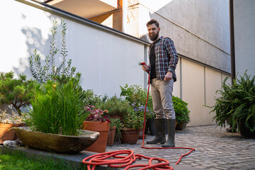 Gardener watering beautiful plants in the garden in front of home, potted flowers watering with a...