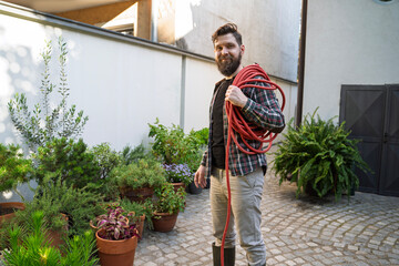Gardener with hose on his shoulder standing by the flowers 