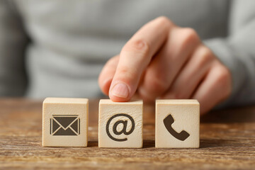 Hand Pointing to Wooden Cube with Email, Phone, and @ Contact Symbols