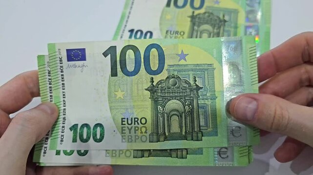Hands holding and counting 100 euro banknotes with stack of cash, close up view of European currency, money handling and payment concept with multiple bills in motion