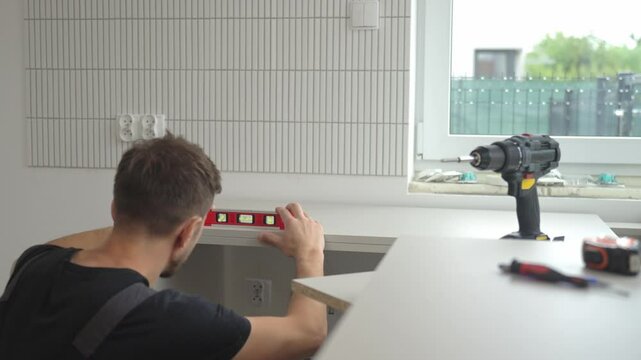 Man uses spirit level to align kitchen countertop panel during installation. Professional kitchen furniture assembly during renovation in new home