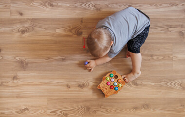 Baby boy playing with wooden fishing toy while sitting on floor at home. Educational activity for fine motor skills development.