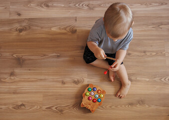 Baby boy playing with wooden fishing toy while sitting on floor at home. Educational activity for fine motor skills development.