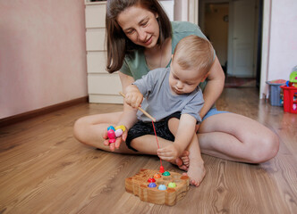 Mother and toddler playing together with a wooden fishing toy at home. Early childhood development and parent-child bonding activity indoors.