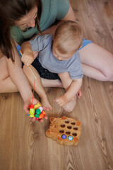 Mother and toddler playing together with a wooden fishing toy at home. Early childhood development and parent-child bonding activity indoors.