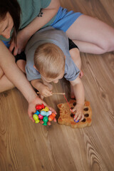Mother and toddler playing together with a wooden fishing toy at home. Early childhood development and parent-child bonding activity indoors.