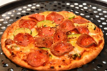 A delicious personal pizza, bubbling with melted cheese, crispy pepperoni, and fresh zucchini, resting on a perforated pizza pan.