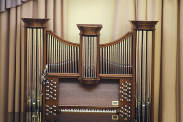 Front view of a traditional pipe organ with polished metal pipes and a wooden console, set against...