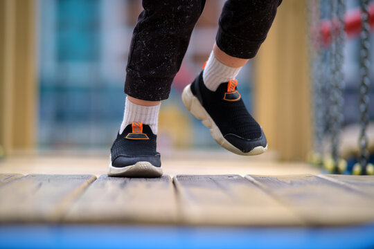 Kid's legs and feet in sneakers on playground background. Child legs walking on wooden planks. Active playful childhood concept. A child aged 3 years