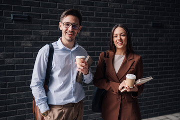 Smiling business people holding disposable coffee cups and books outdoors
