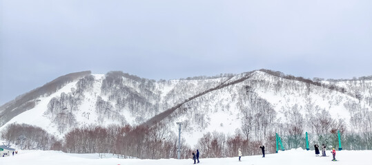 Snow mountains and hills covered with snow in winter under cloudy sky in Japan with unrecognized tourists