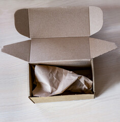 Open kraft cardboard box filled with crumpled brown paper filler on wooden surfaces, eco-friendly packaging ,sustainability, biodegradability, responsible shipping, logistics and online retail
