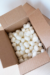 Open cardboard box filled with eco-friendly corn-based packing peanuts on a light wooden surface. Sustainable packaging for safe and conscious shipping, promoting zero-waste