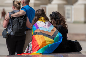 Couple of girls with rainbow coloured flag and heterosexual couple hugging during a LGBT+ pride parade