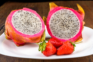 Two halves of dragon fruit or pitahaya and three strawberries on a white plate.