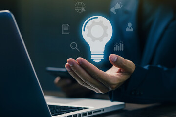 A businessman holding a glowing lightbulb with digital business icons, symbolizing innovation, creative ideas, business strategy, and technology-driven solutions.