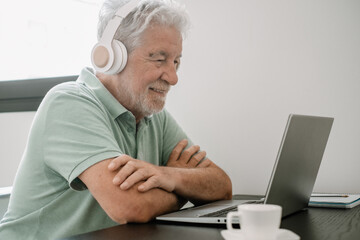 Video call concept.  Senior caucasian smiling businessman sitting at home desk working online on laptop, enjoying a coffee cup