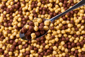 metal spoon of corn balls above tasty chocolate corn balls as background. Top view.