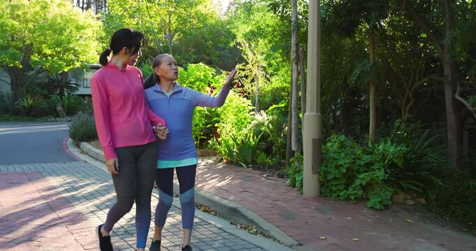 Linking arms Chinese mom and daughter walking on brick pathway pointing at trees to admire scenery