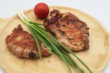 Grilled pork steak served with green onions and fresh tomatoes
