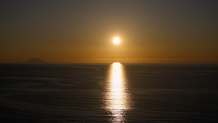 Golden sunset over Tyrrhenian Sea with Stromboli volcano silhouette and sun reflecting on water surface