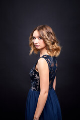 Fototapeta premium A woman in a black dress poses in a studio against a dark background. She has a beautiful athletic figure.