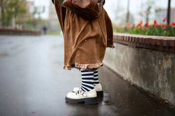 Young woman's legs in white sandals and warm brown corduroy skirt stepping through early spring snow, showcasing seasonal contrast