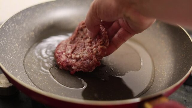 Horizontal 4K video close up. Male hand places round burger patty, cutlet on frying pan. Ground beef, meat, pork, lamb is fried in oil. Health food preparation process. No vegan cafe. Man cooks dinner