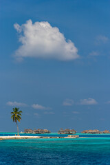 Island with bungalows floats on turquoise sea.