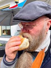 bärtiger Mann genießt ein Fischbrötchen mit Hering