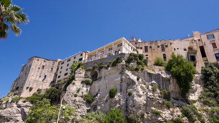 Fototapeta premium White and yellow buildings standing on a cliff overlooking the sea in Tropea, Calabria, Southern Italy, under a clear blue sky