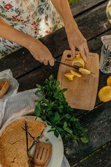 Outdoor summer picnic scene with a homemade lemon poppy seed pie, fresh lemons, mint, and lemonade on a rustic wooden table in a garden setting. Cozy and vibrant natural atmosphere.