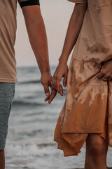 Romantic seaside moments. A couple holds hands near the ocean and enjoys a cozy beach picnic with fresh fruits and a sparkling drink at sunset.