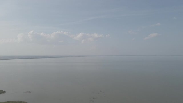 Drone based aerial fling high above a large lake under a hazy blue sky with scattered clouds.