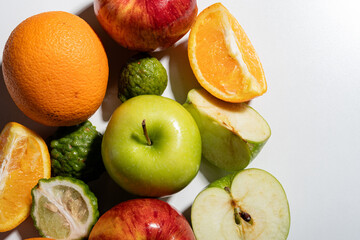 Close-up of mixed fresh fruits with apples, orange slices, and kaffir limes on white background