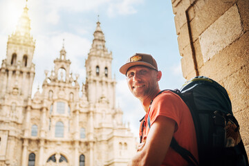 Joyful smiling middle-aged backpacker pilgrim sitting on Obradoiro square in Santiago de...