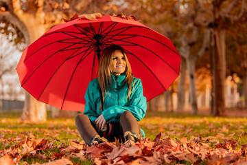 Woman sitting under a red umbrella surrounded by autumn leaves. Lifestyle. Autumn.