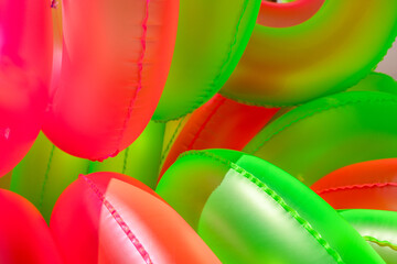 Colorful inflatable swim rings in vibrant pink and green shades are stacked together, perfect for a lively day at the pool or beach party during the sunny summer season.